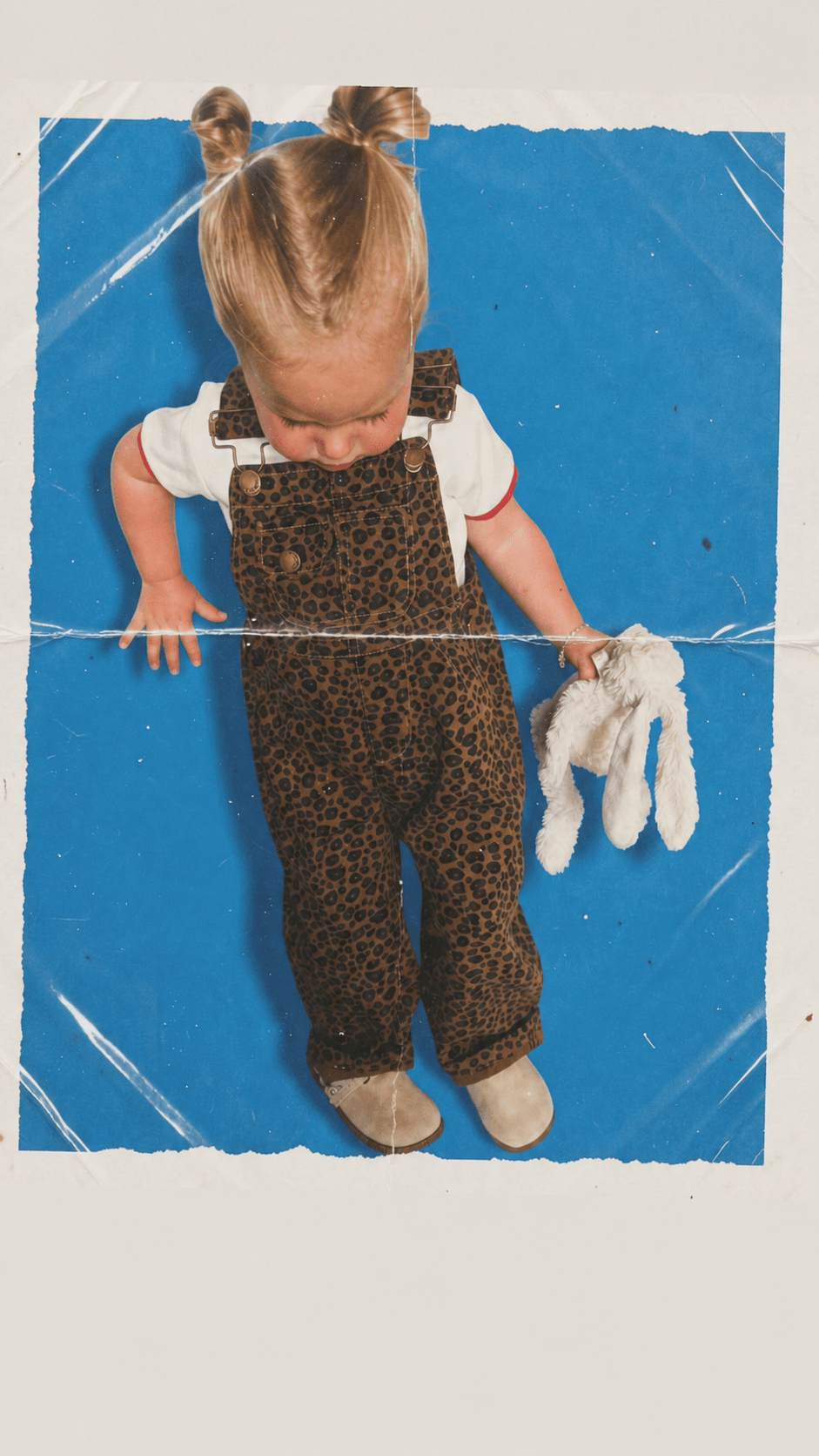 Child wearing Route B leopard dungarees on a blue paper background