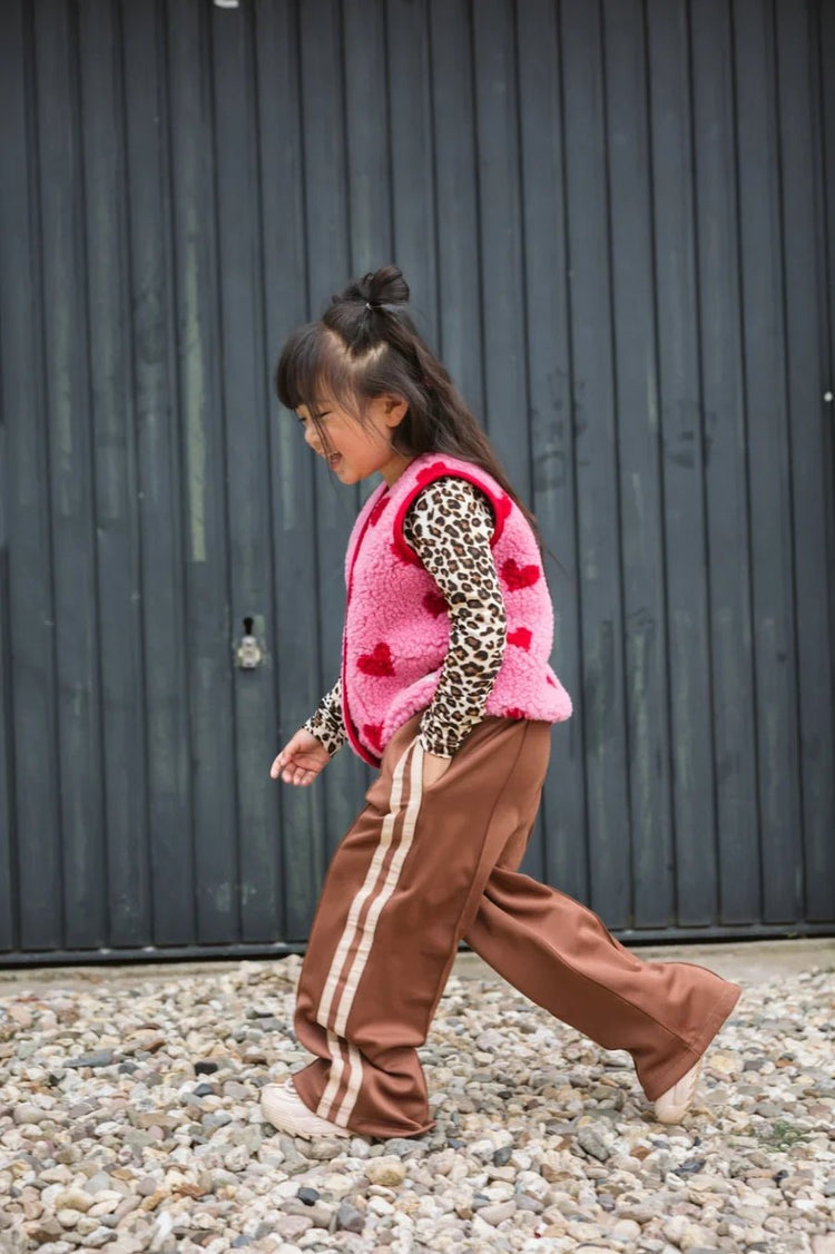 Kind trägt braune Hose und pinke Wollweste von Salty Stitch x Alwero