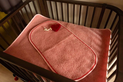 We Are Wovens wollen onderlegger voor baby’s in roze in babybed