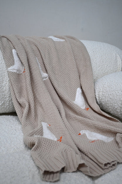 Beige Gordy Goose babydeken met witte gans van Lennyco op een bank
