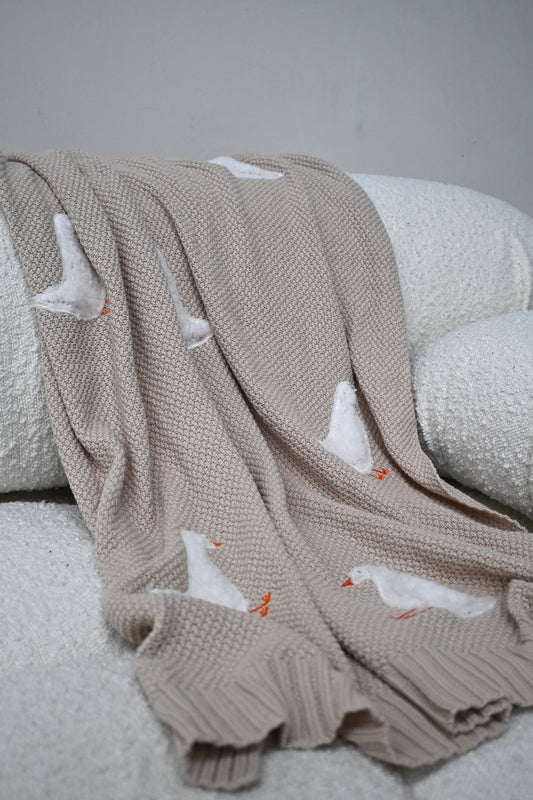 Beige Gordy Goose Babydecke mit weißem Gänsemotiv von Lennyco auf einem Sofa