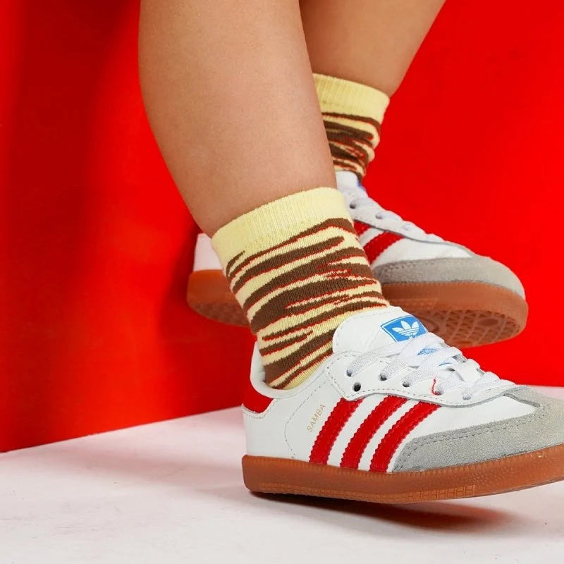 Kind draagt gestreepte Vesper sokken van The New Chapter met rode sneakers